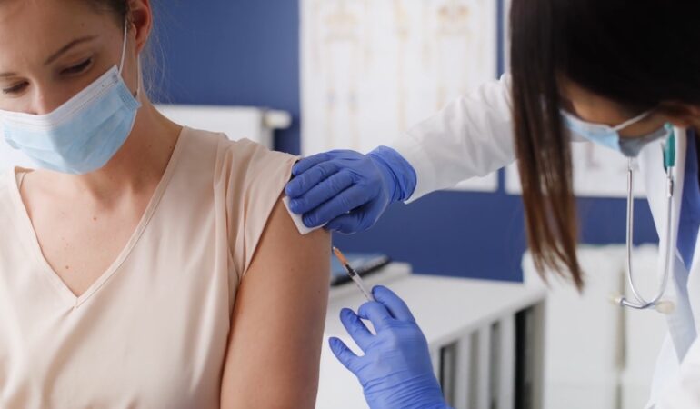 Doctor giving a vaccine injection to an adult woman in a clinic setting
