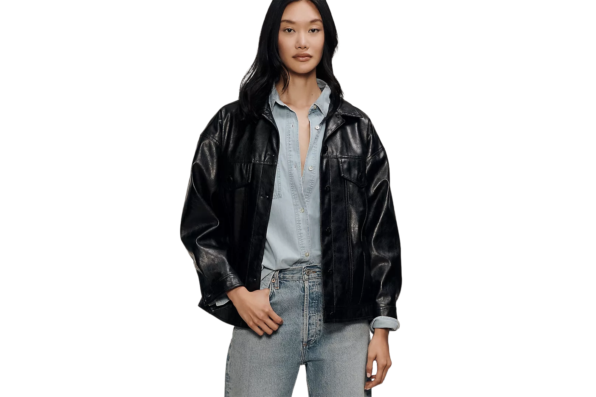 A woman wears a black leather jacket over a light blue denim shirt and light wash jeans.