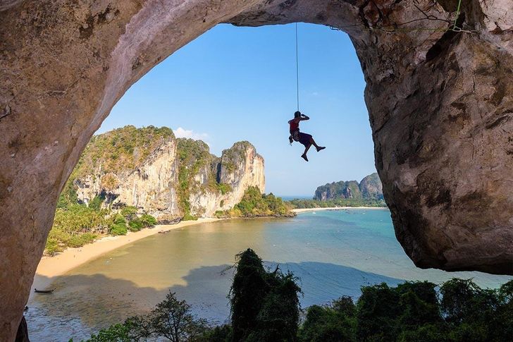 A climber dangles from a limestone cliff above the turquoise waters and golden shoreline of Krabi, Thailand.  Courtesy of Tourism Authority of Thailand