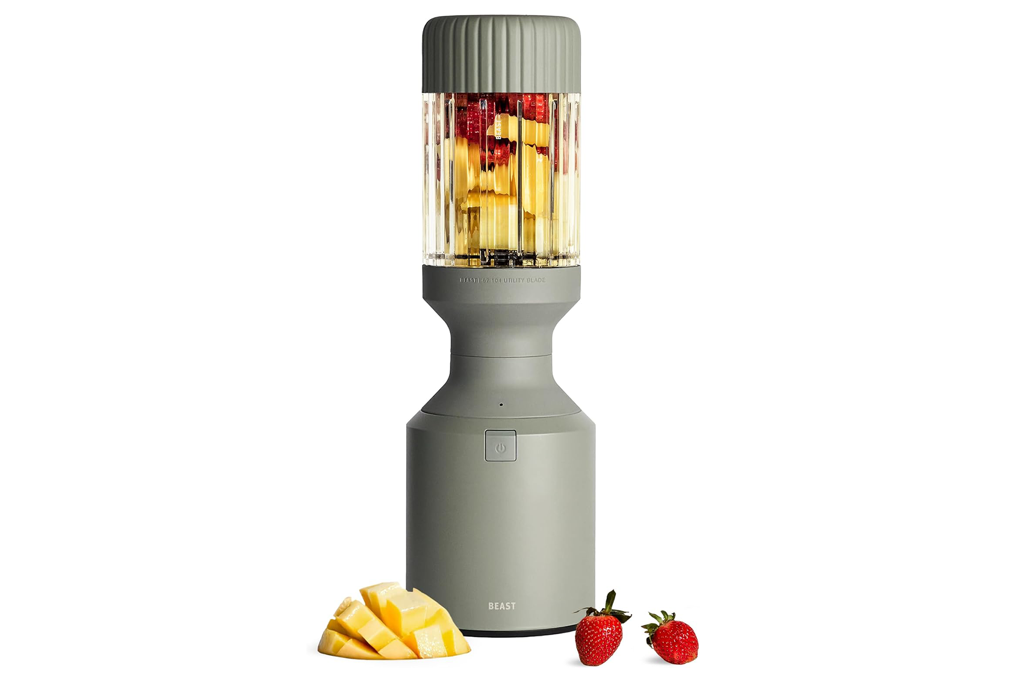 A grey Beast blender with fruit in the blending cup, with sliced mango and two strawberries in front.