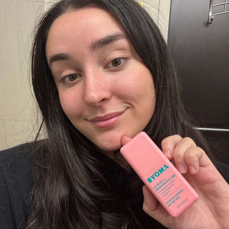 Cusack holding the Byoma Eye Gel in her left hand in front of a wall.