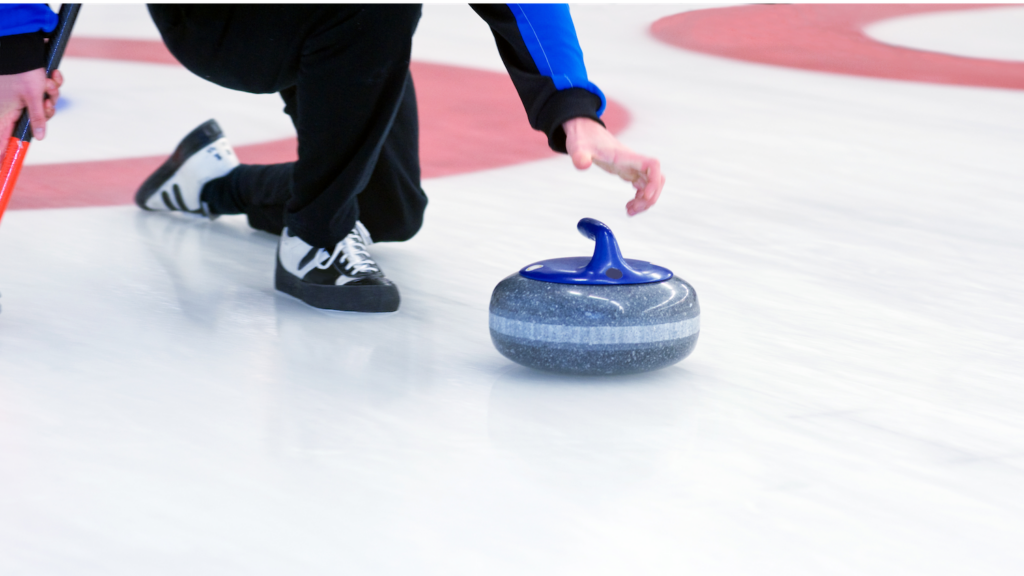 A curling stone with a blue handle sliding on ice, guided by a crouching player.