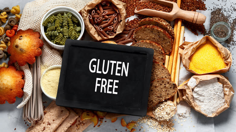 A sign that says gluten free, with various ingredients in the background, including uncooked pasta, bread, and other grains.