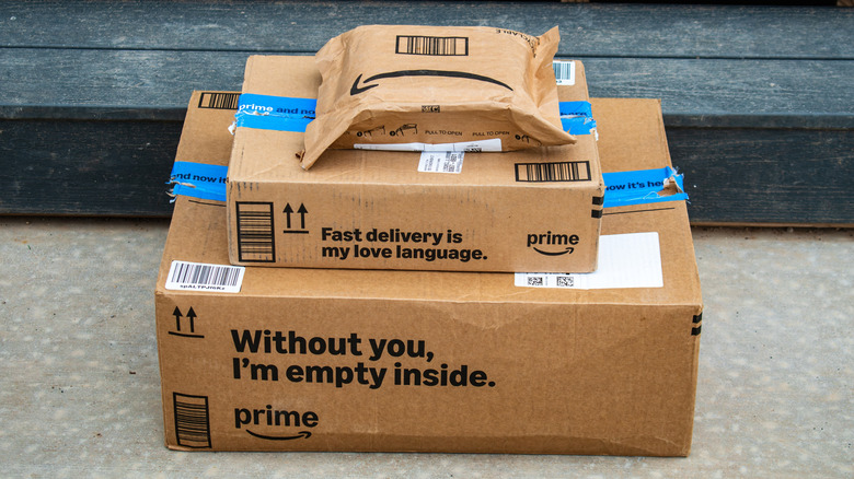 Three amazon packages of various sizes sit atop one another on a porch in front of a step