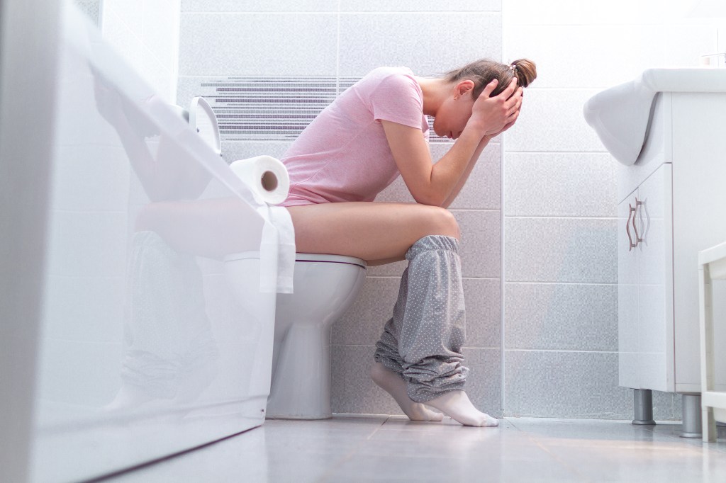 Woman on a toilet in distress, holding her head in her hands.