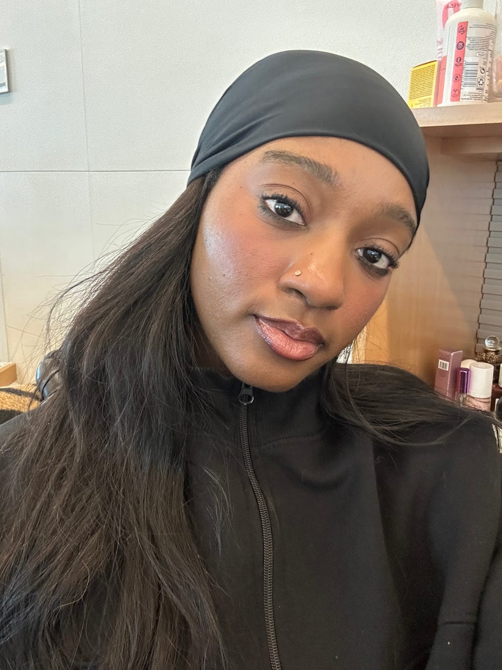 person with long hair wearing a black jacket and head covering with a blurred face