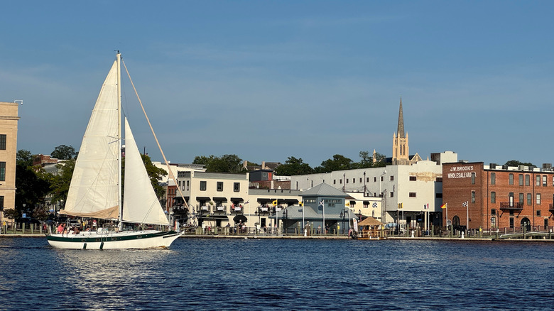 A sailing boat cruising down the river alongside Wilmington's historic downtown buildings.