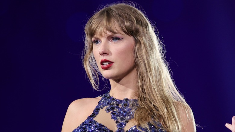 Taylor Swift performing on stage in a blue bodysuit with a blue background