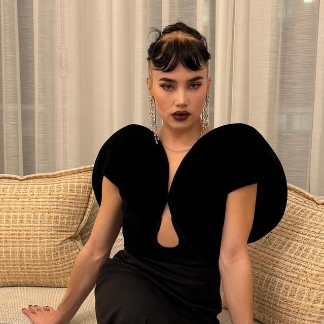 a person wearing an elegant black dress with distinctive shoulder designs seated on a couch