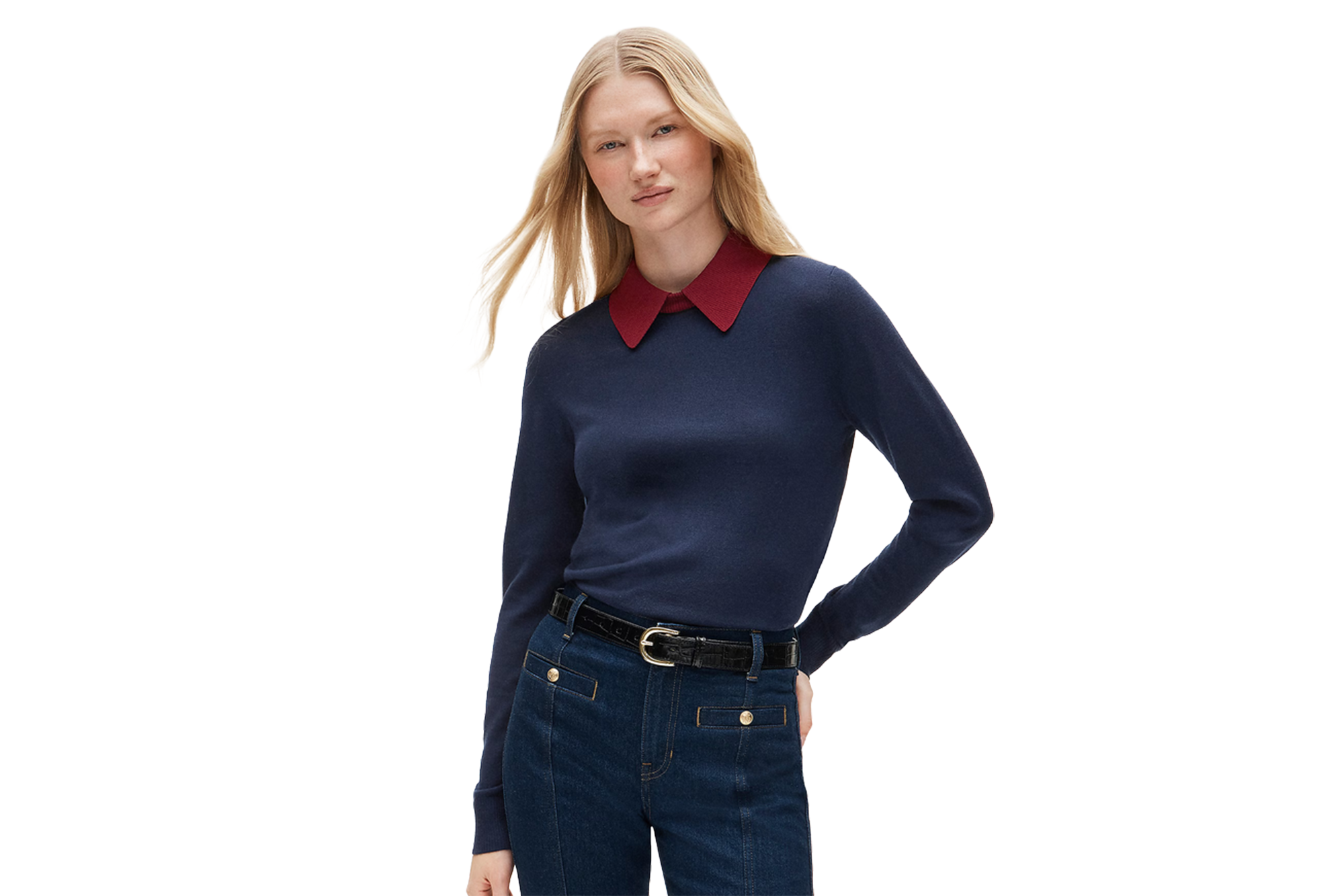Woman wearing a navy sweater with a red collar, dark wash jeans with gold buttons, and a black belt.