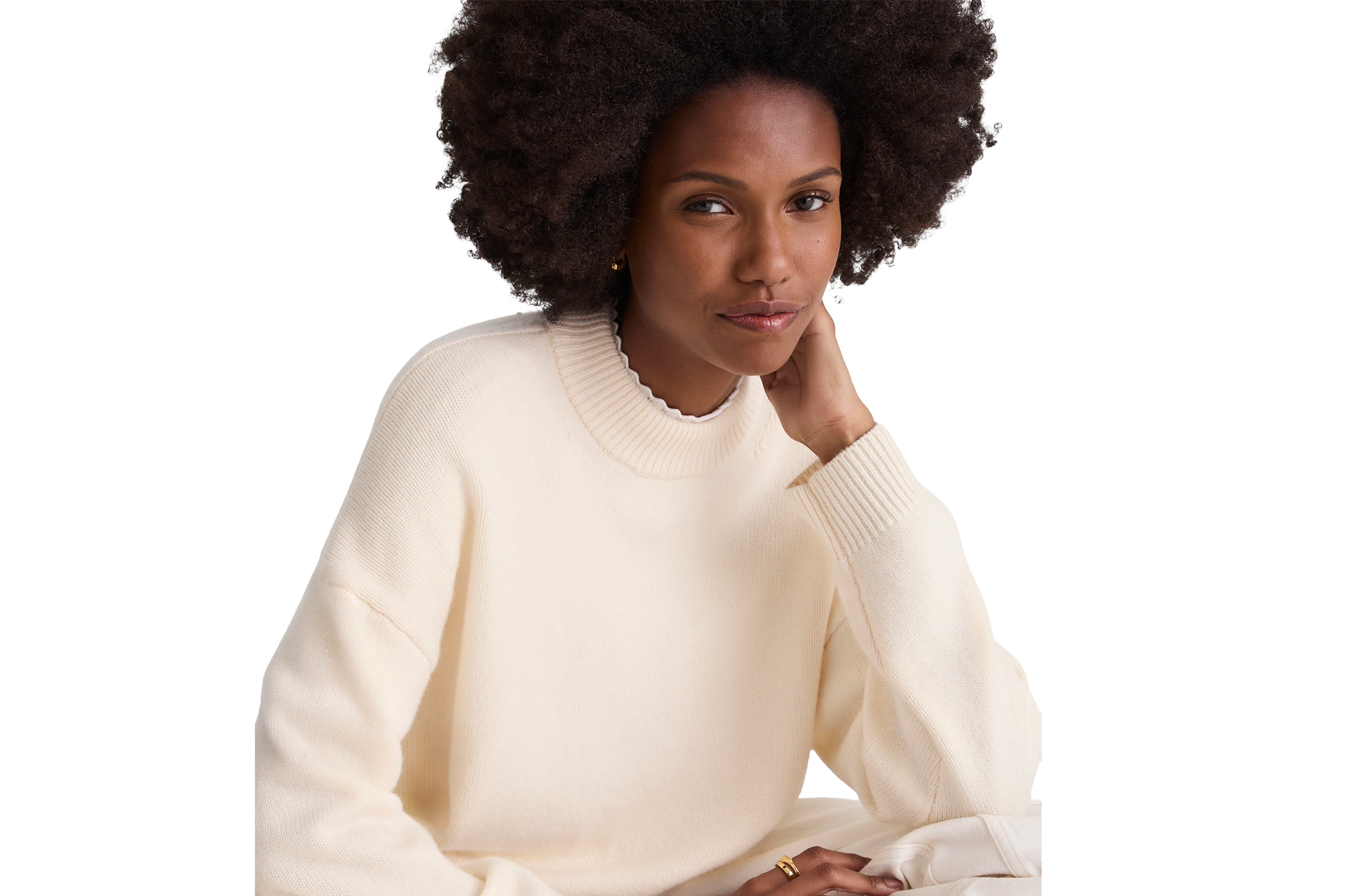 A woman with dark curly hair wearing a cream-colored sweater.
