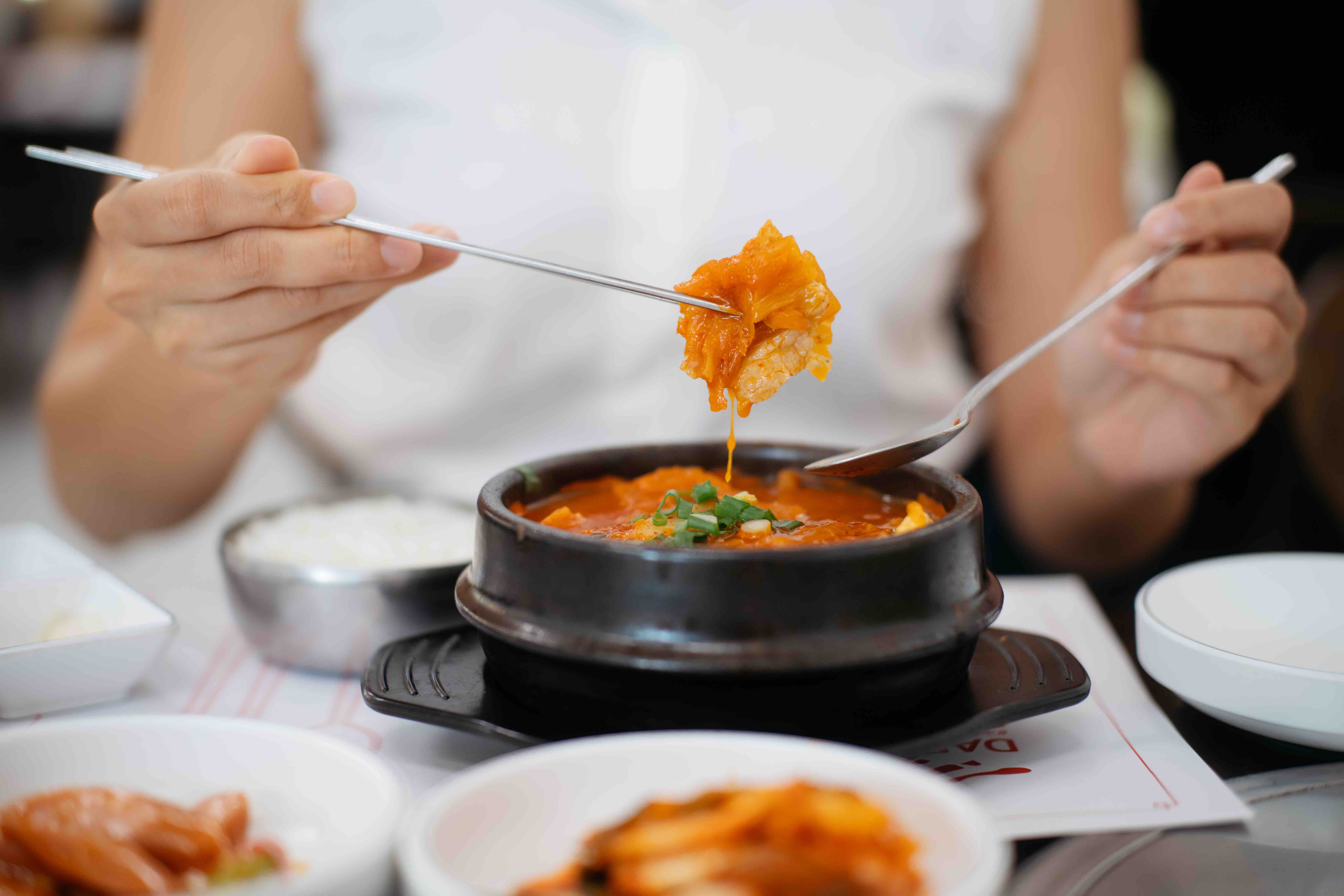 Asian woman enjoying Korean kimchi soup and tableful of side dishes