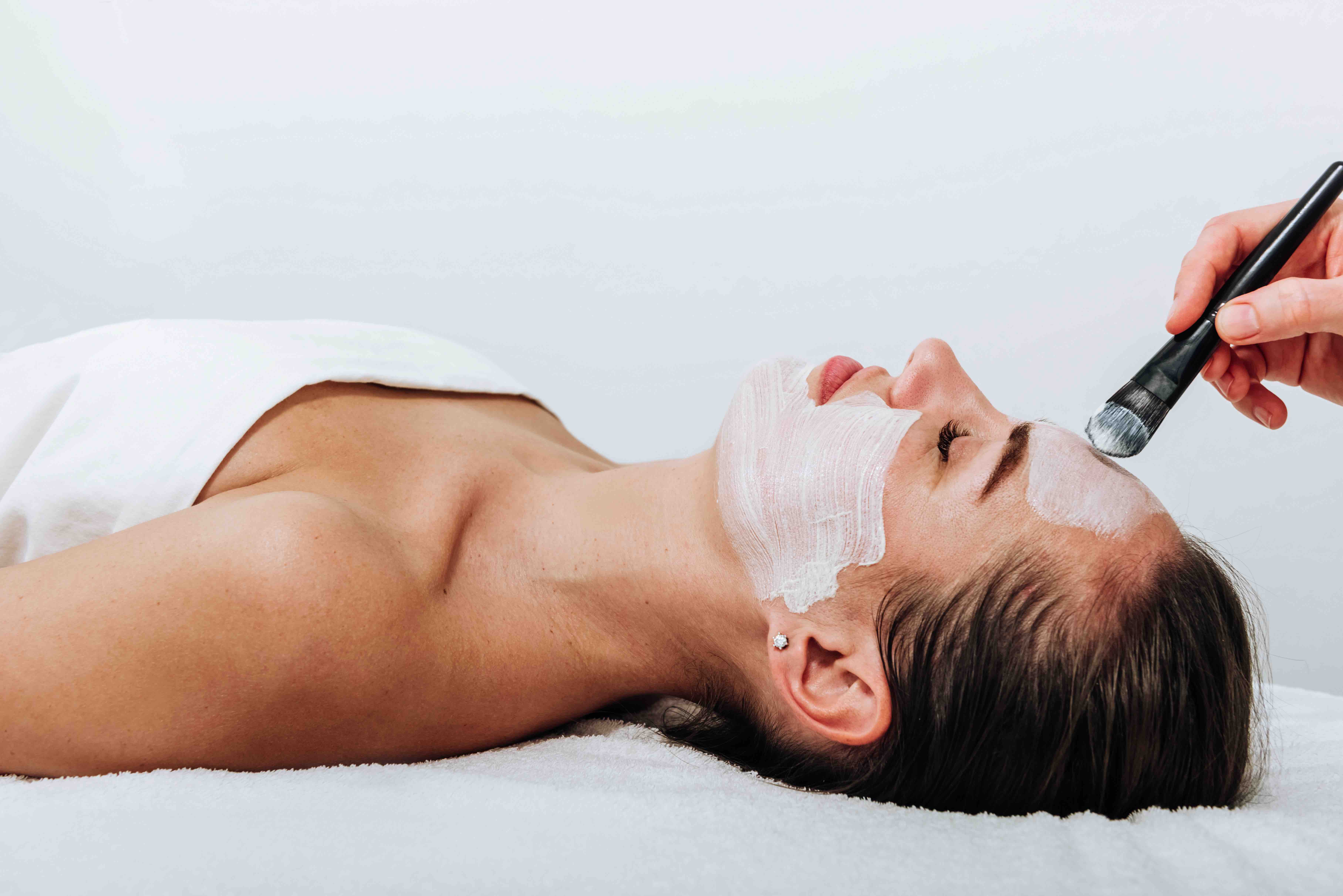 beauty mask applied to a woman's face with a brush by a cosmetologist