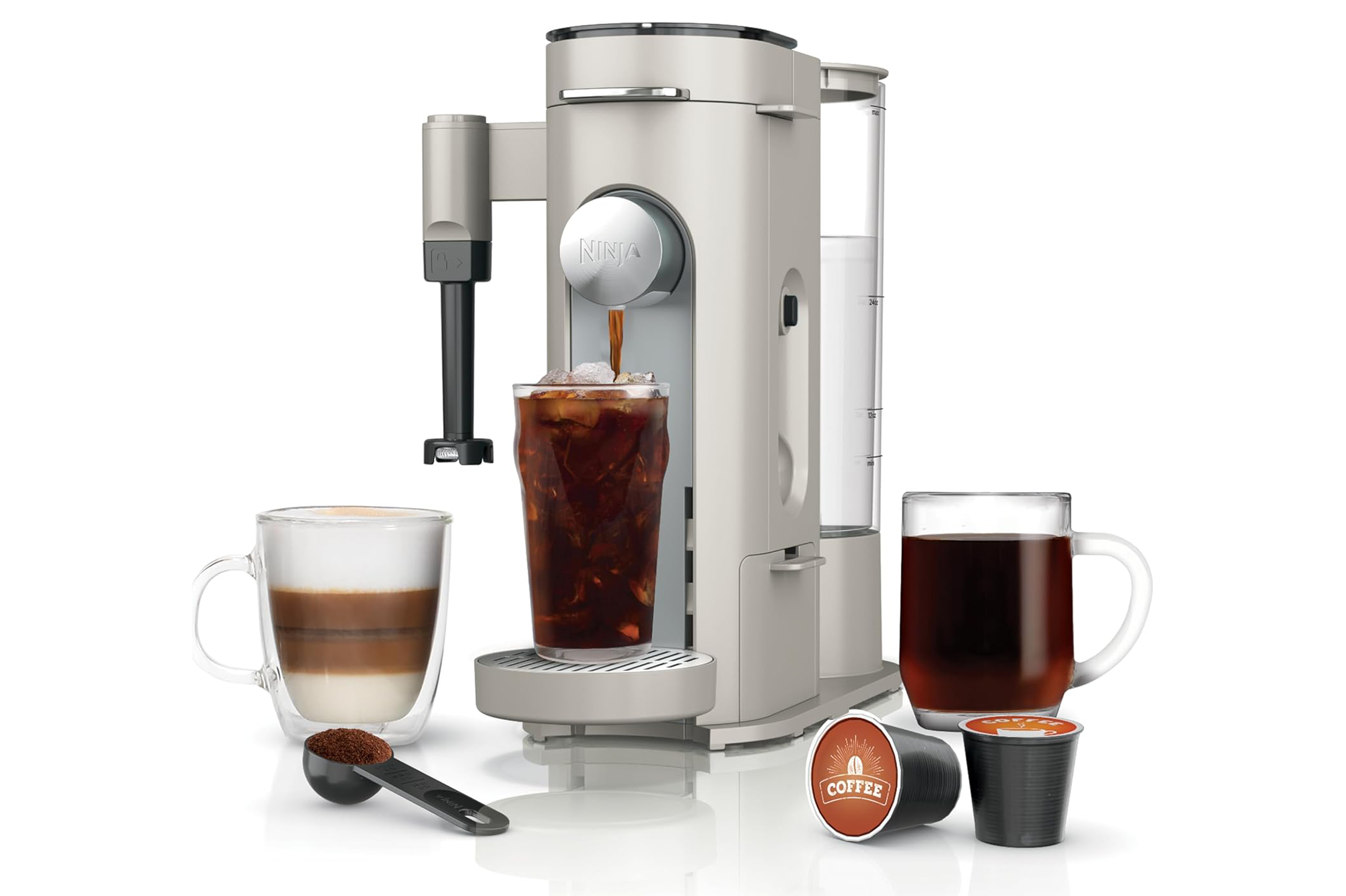 Ninja coffee maker with coffee brewing into a glass of iced coffee, a latte, and a mug of black coffee, along with coffee pods and ground coffee.