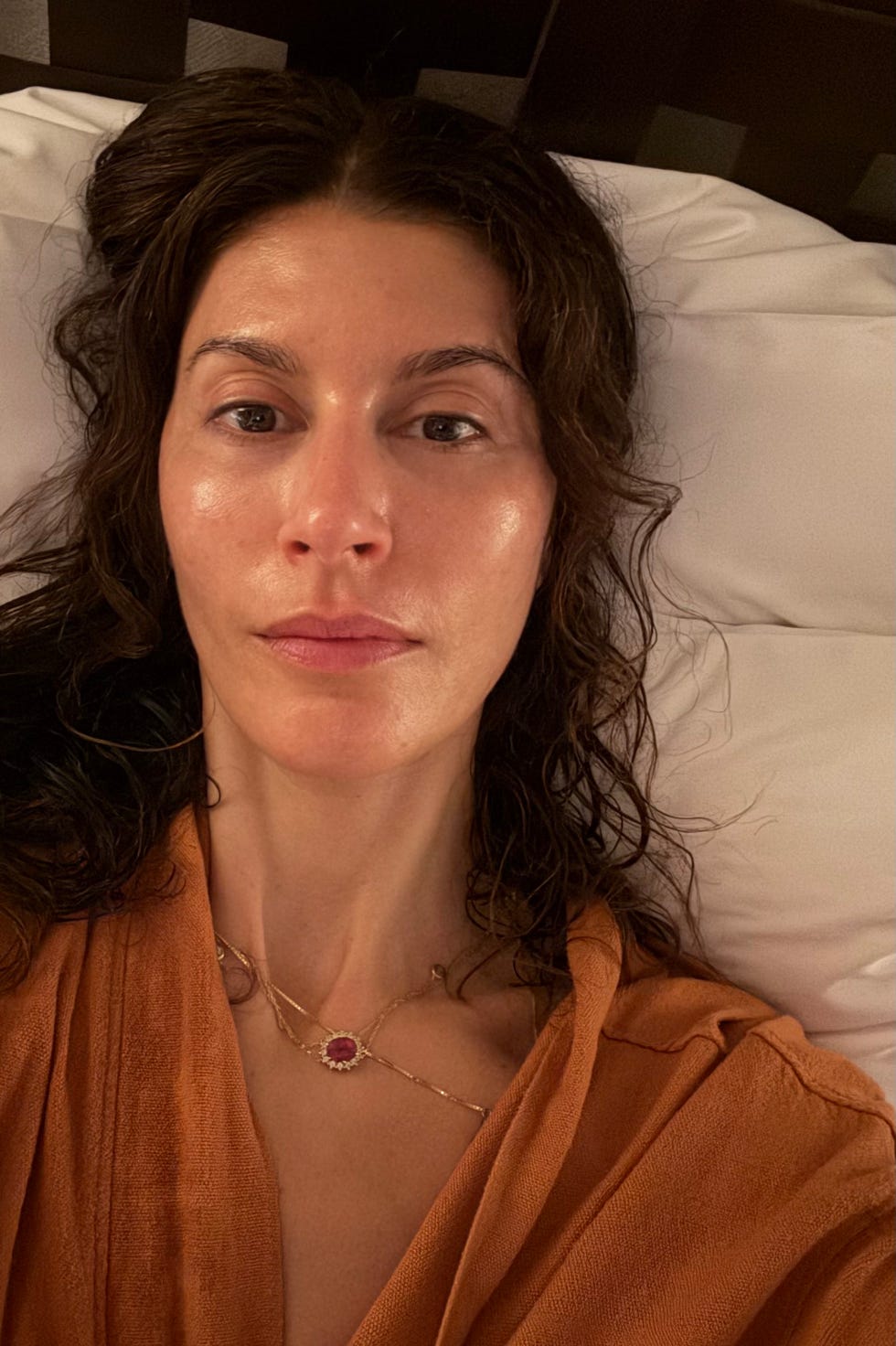 person resting on a bed with curly hair and wearing an orange garment