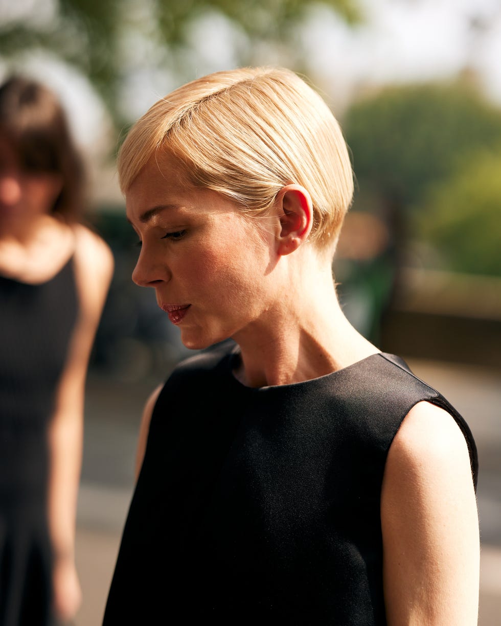 two individuals one in focus wearing a black dress and with short blonde hair