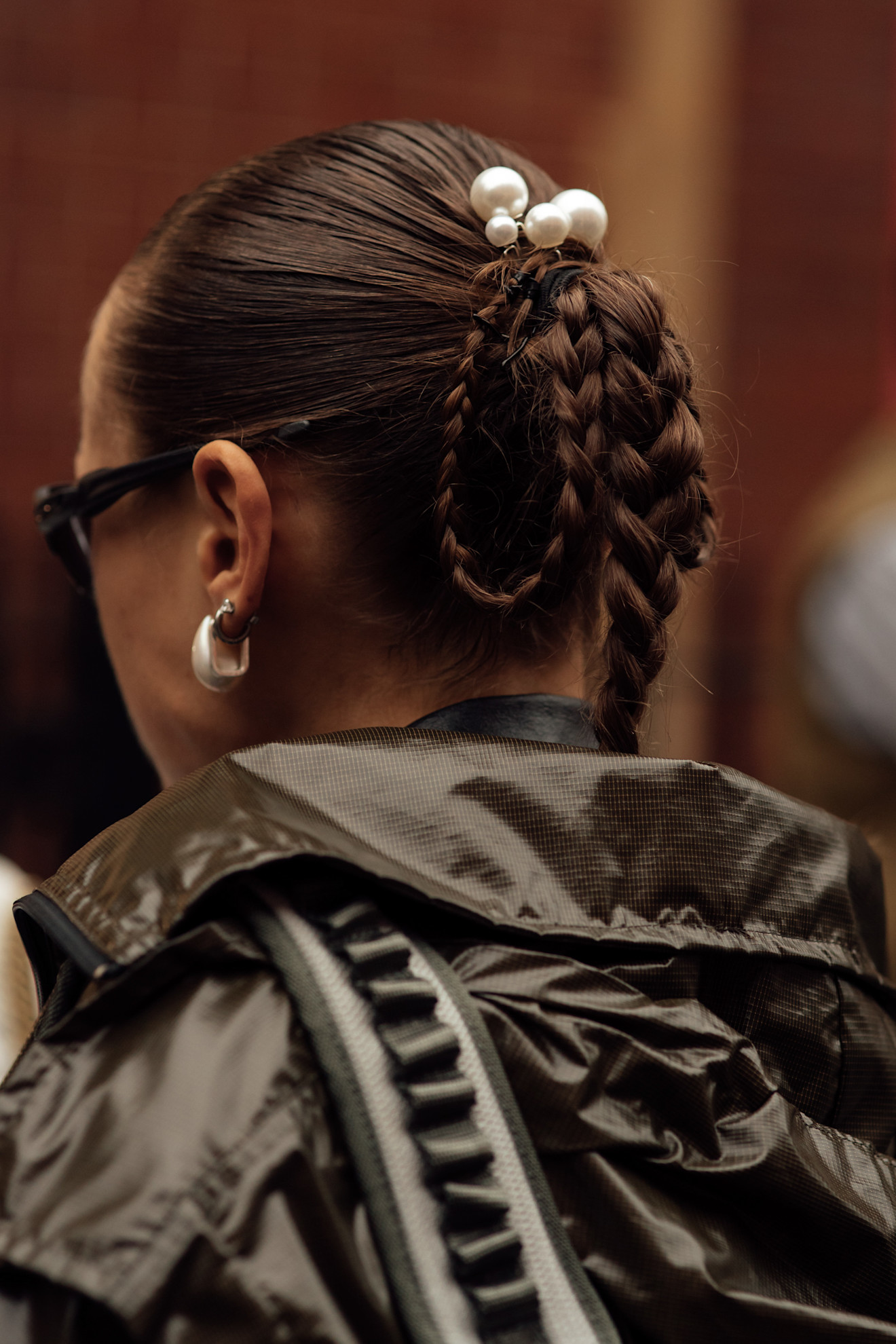 A close-up of a ponytail, slicked back and finished with plaits and pearl hair accessories