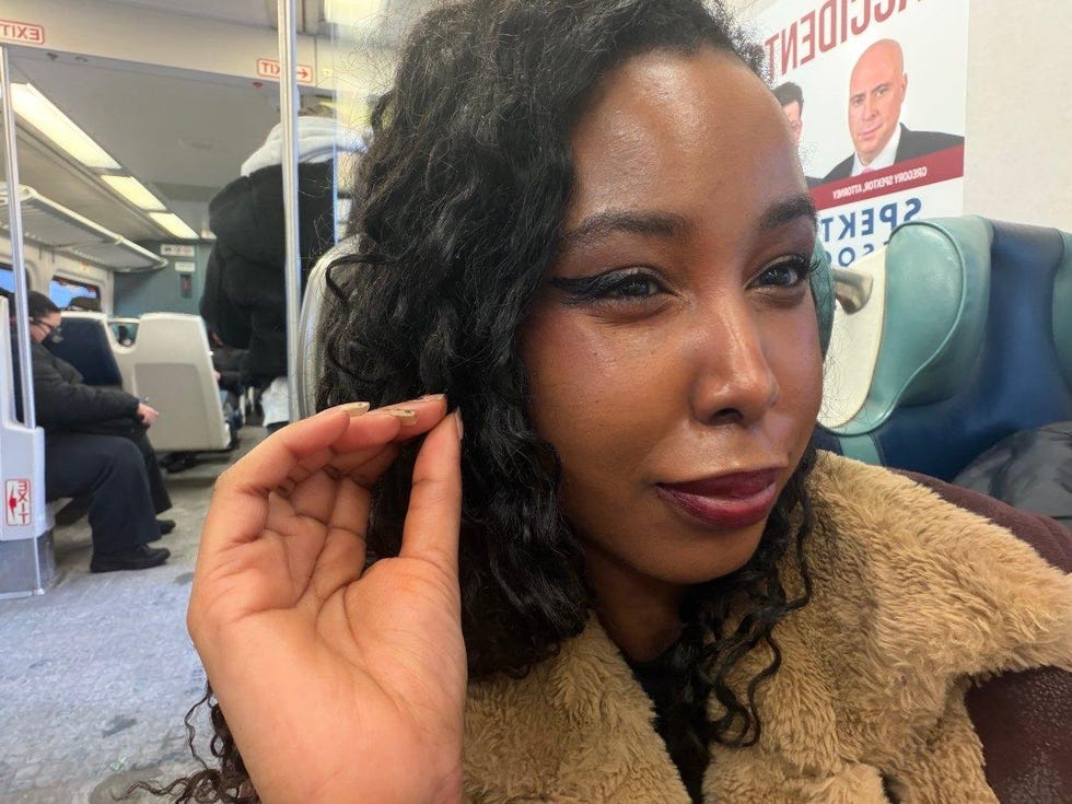 a person sitting in public transportation with curly hair and a hand near their face