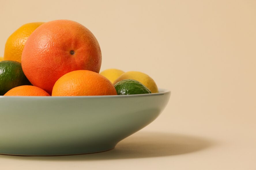 Image of a green bowl filled with various citrus fruits, including oranges, lemons, and limes.