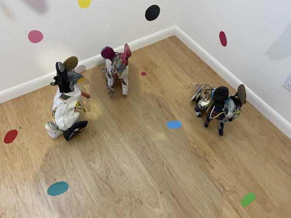 A detail photograph of an installation by Ken Little and Cathy Cunningham-Little featuring a trio of sculptured rabbits on a wooden floor with small colorful mirrored circles throughout the space.