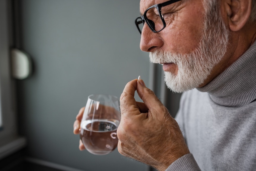 Older man holding a glass of water and a vitamin tablet.
