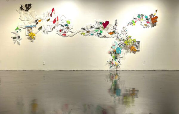 An installation image of a large multipart artwork featuring an array of hand-cut materials assembled on a gallery wall.