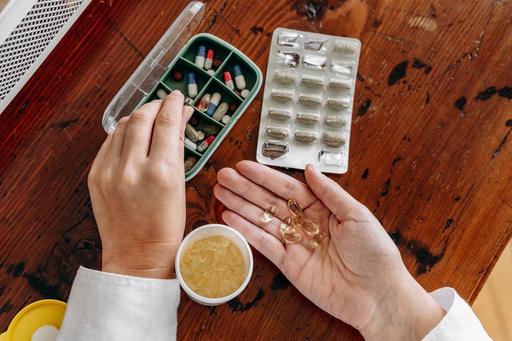 A pair of hands sorts capsules and tablets, with a white medication bottle and a divided pill organizer on a wooden table. This stock image captures everyday health management and medication organization.