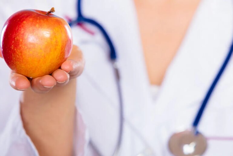 A photo of a female physician holding an apple.