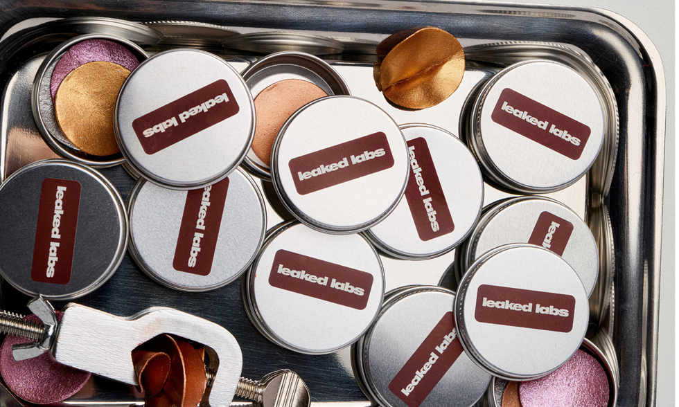 Cosmetic tins with varying colors of makeup inside, some lids off.