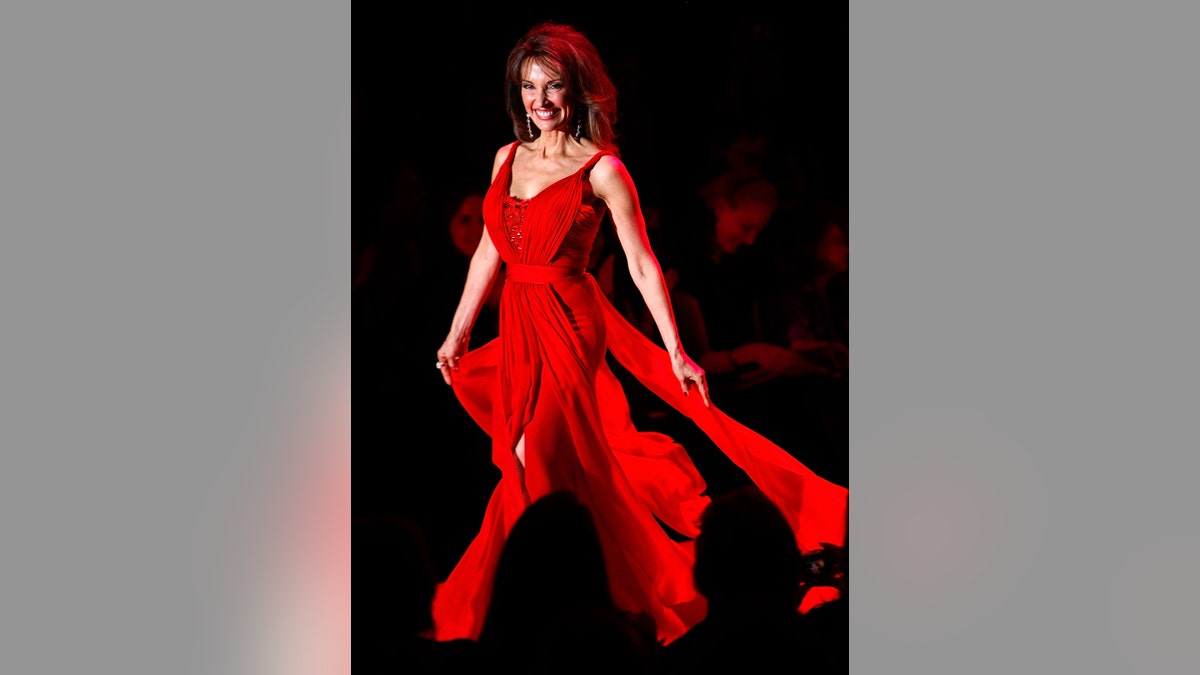 Susan Lucci walking on the runway wearing a red gown.