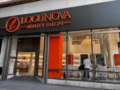 The exterior of Logunova Beauty Salon features a modern storefront with high-visibility orange branding against a sleek dark facade. Located at 607 South Olive, the salon offers an inviting atmosphere highlighted by large floor-to-ceiling windows and an e