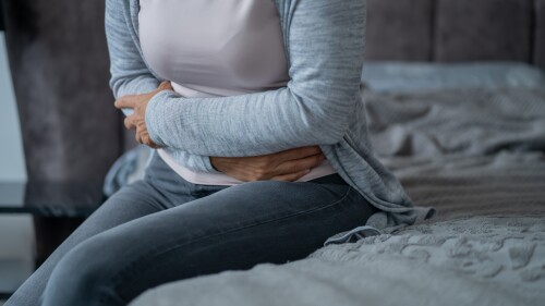 Woman experiencing abdominal pain holding stomach while sitting