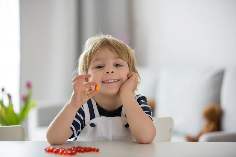 Cute little child, toddler boy, eating alfa omega 3 child supplement vitamin pills at home for better immunity