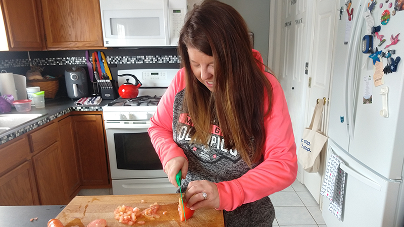 A woman chops a tomato on a cutting board. 