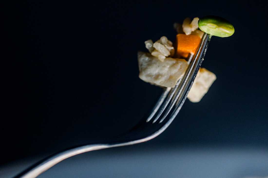 A close up photo shows a bit of chicken, rice, carrot and edamame on a fork.
