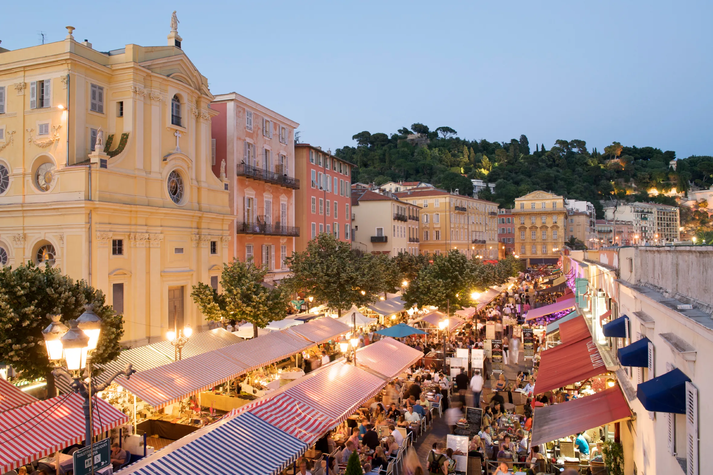 A dusk view of the Cours Saleya with tourists dining in outdoor cafes.