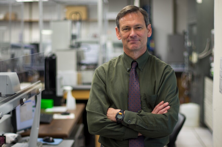 A middle-aged man poses with his arms crossed in a scientific lab