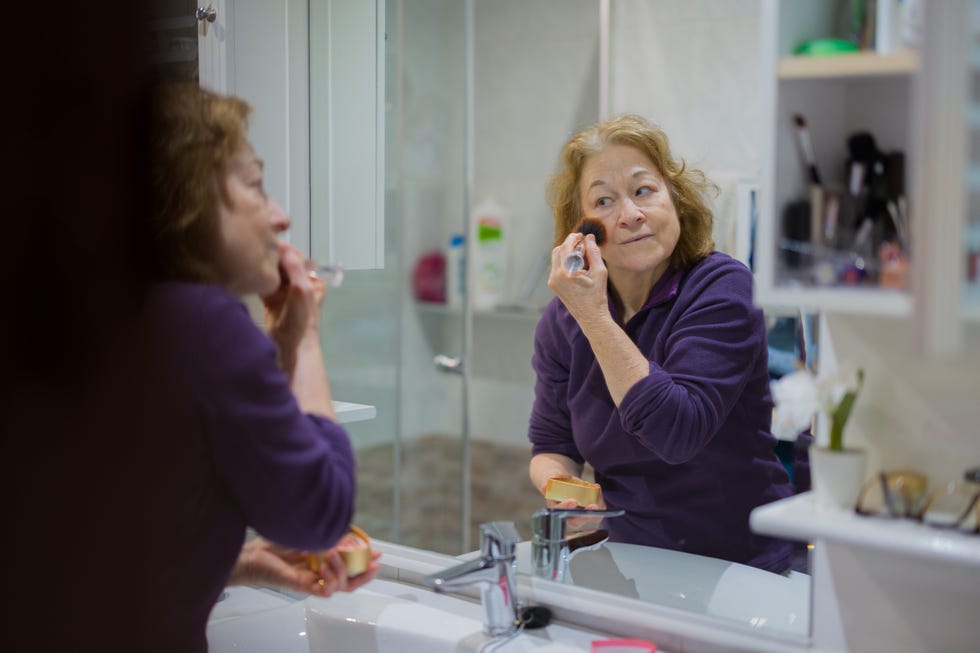 Makeup History Facts You Should Know But Don't  Senior woman applying makeup in the bathroom mirror