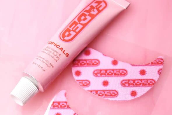 A tube of pink cosmetic cream with red text is placed on a pink surface. Adjacent to it is a pink, polka-dot circular object.