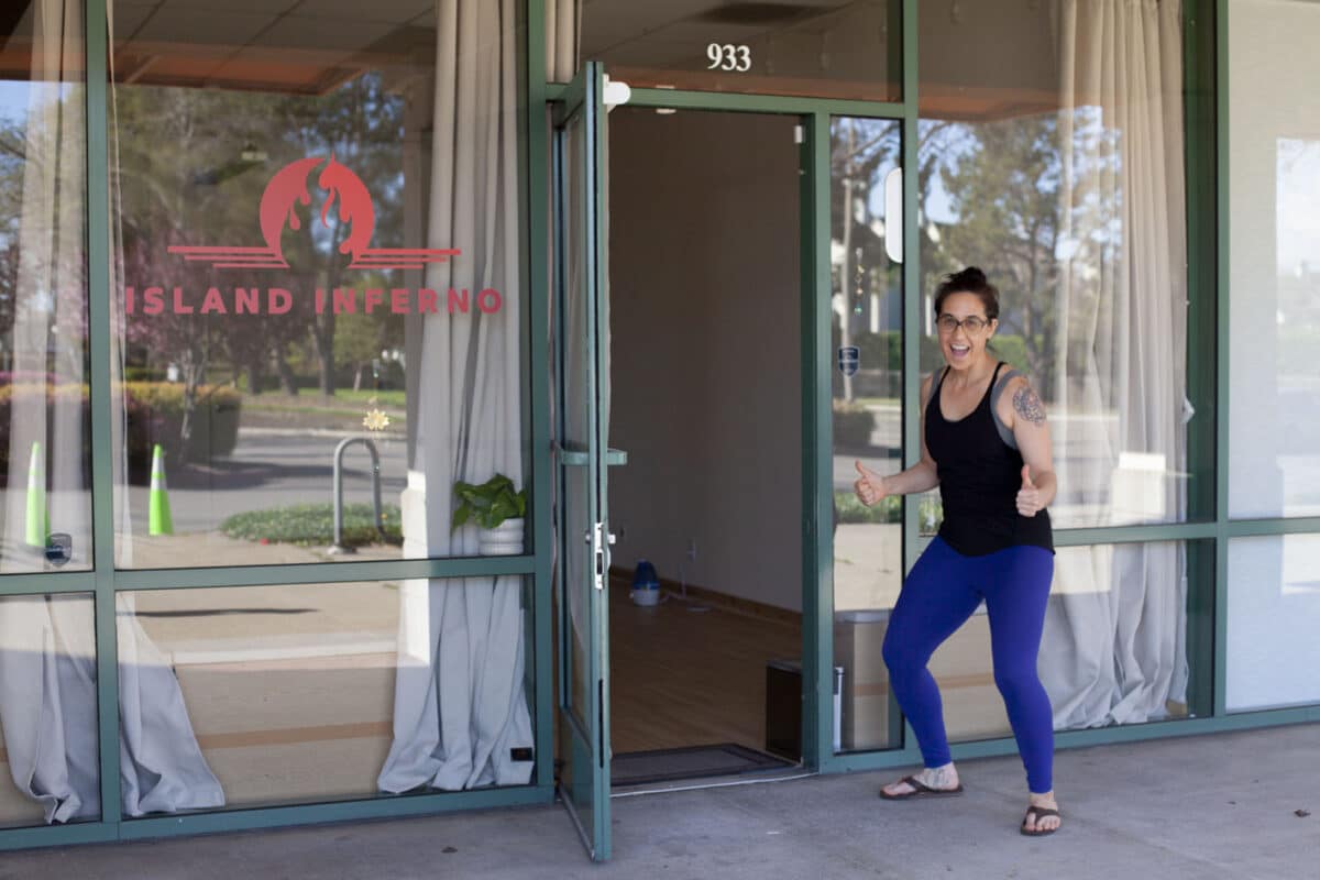 Alameda Post - A woman stands outside the door to Island Inferno and holds a thumbs up. 