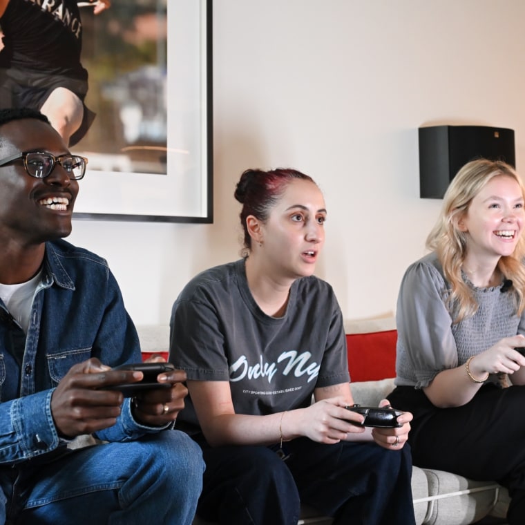 A photo of three people sitting on a couch holding different Nintendo Switch controllers, playing a game.