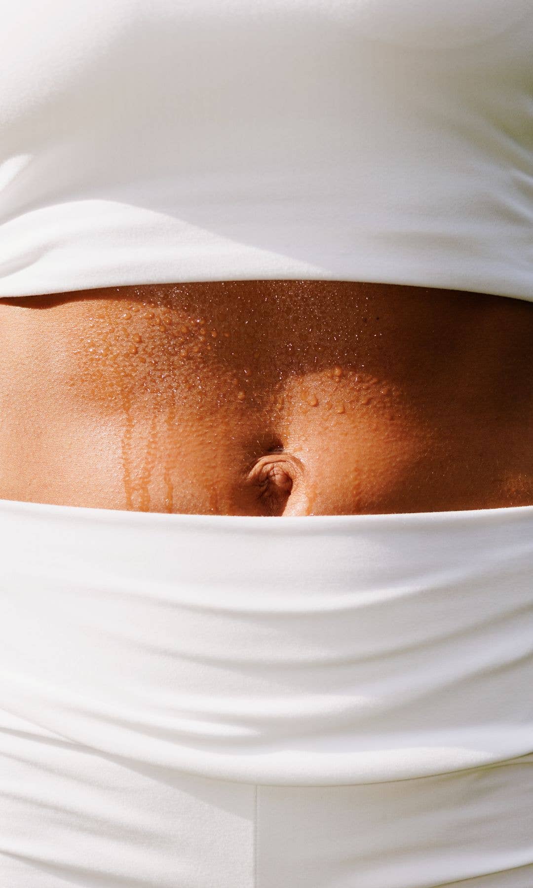 Picture of a stomach with sweat on it and a white a crop top and leggings
