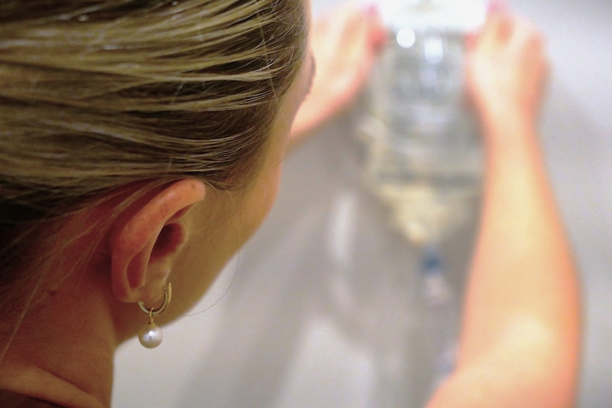 The back of a woman's head as she hangs an IV drip bag on a wall.