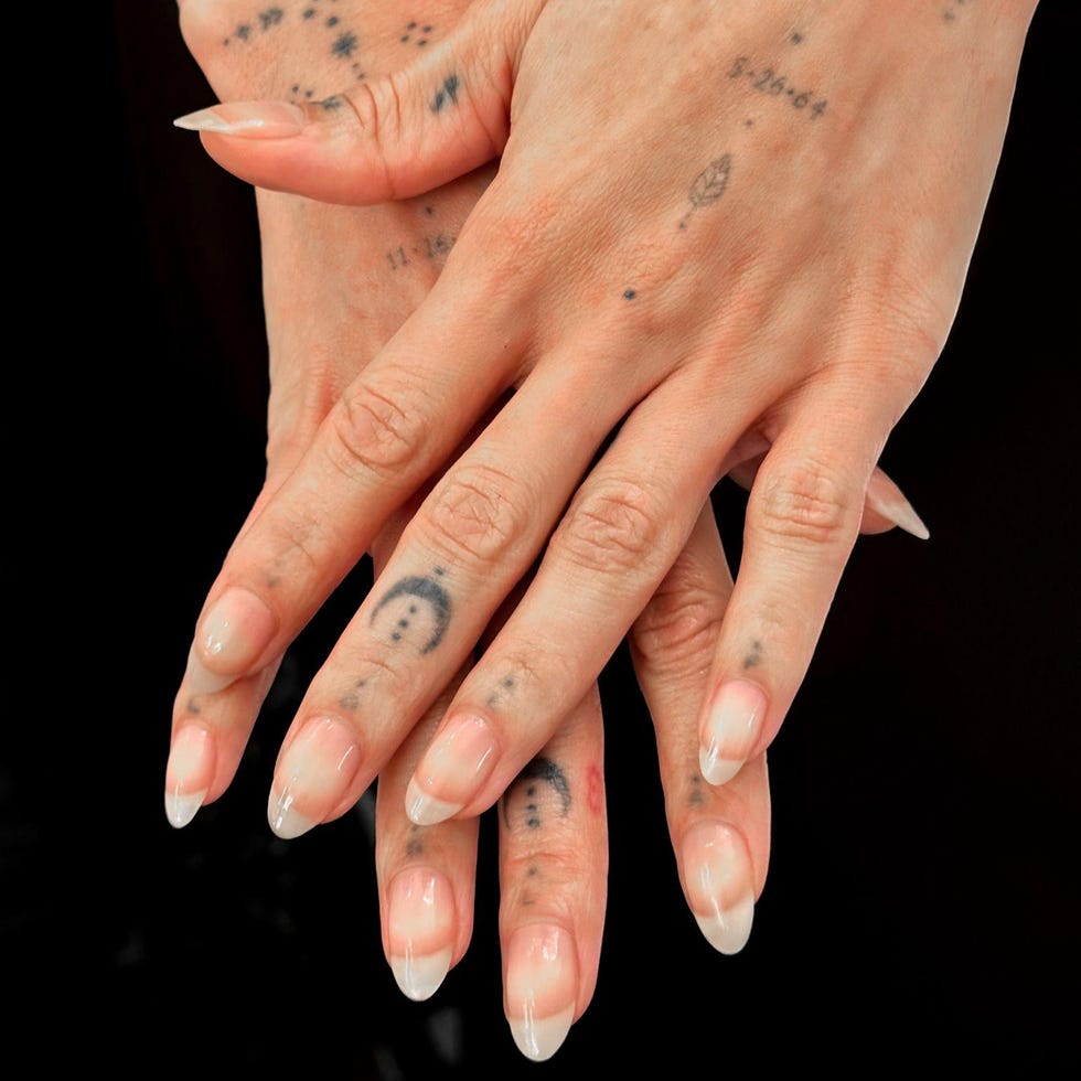 Hands adorned with various tattoos and long, polished nails.