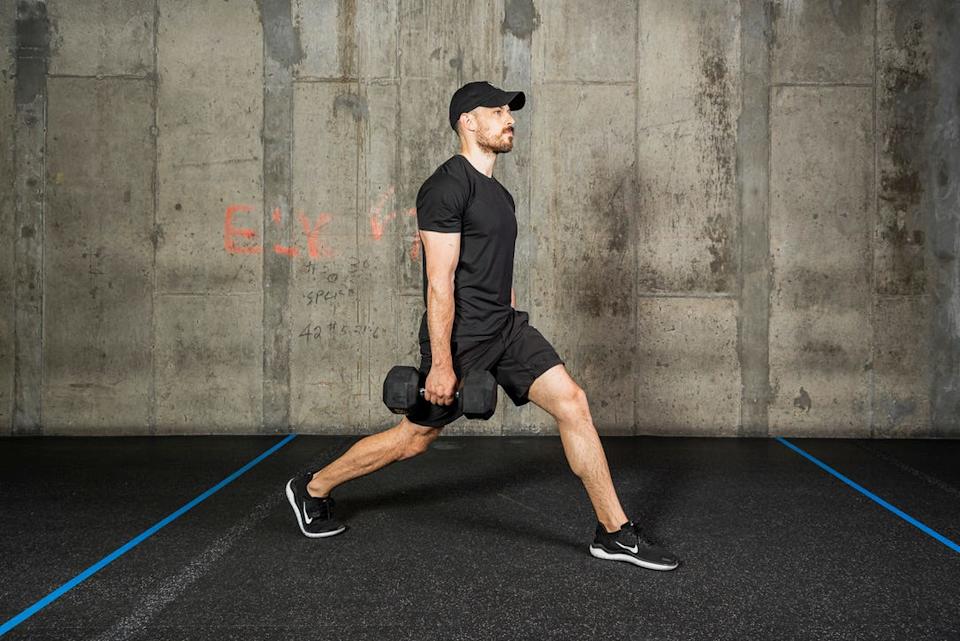 A personal trainer performs a weighted exercise in a gym with dumbbells
