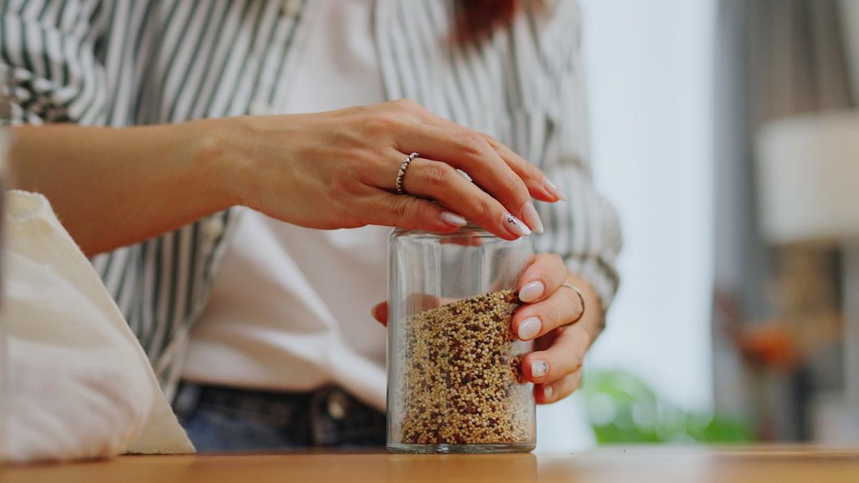 close up hand refilling glass jar containers with quinoa healthy eating,buying organic grains with reusable natural zero waste eco friendly sustainable food packaging eco friendly in sustainable plastic free grocery store