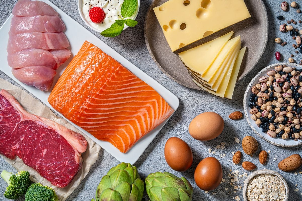 Assorted healthy protein source food good for body building ingredients as: salmon, chicken, beef, fish, eggs, beans legumes and nuts, artichoke, broccoli, cheese, yogurt, and eggs.