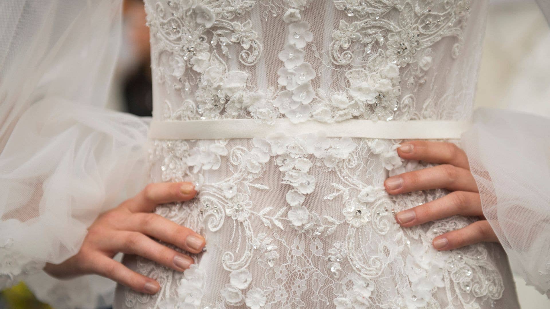 Hands on a model's hips who is wearing a wedding dress backstage at a bridal show