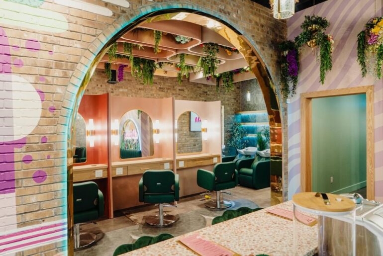 A beauty salon with a colorful brick arch and green seats in front of lit mirrors