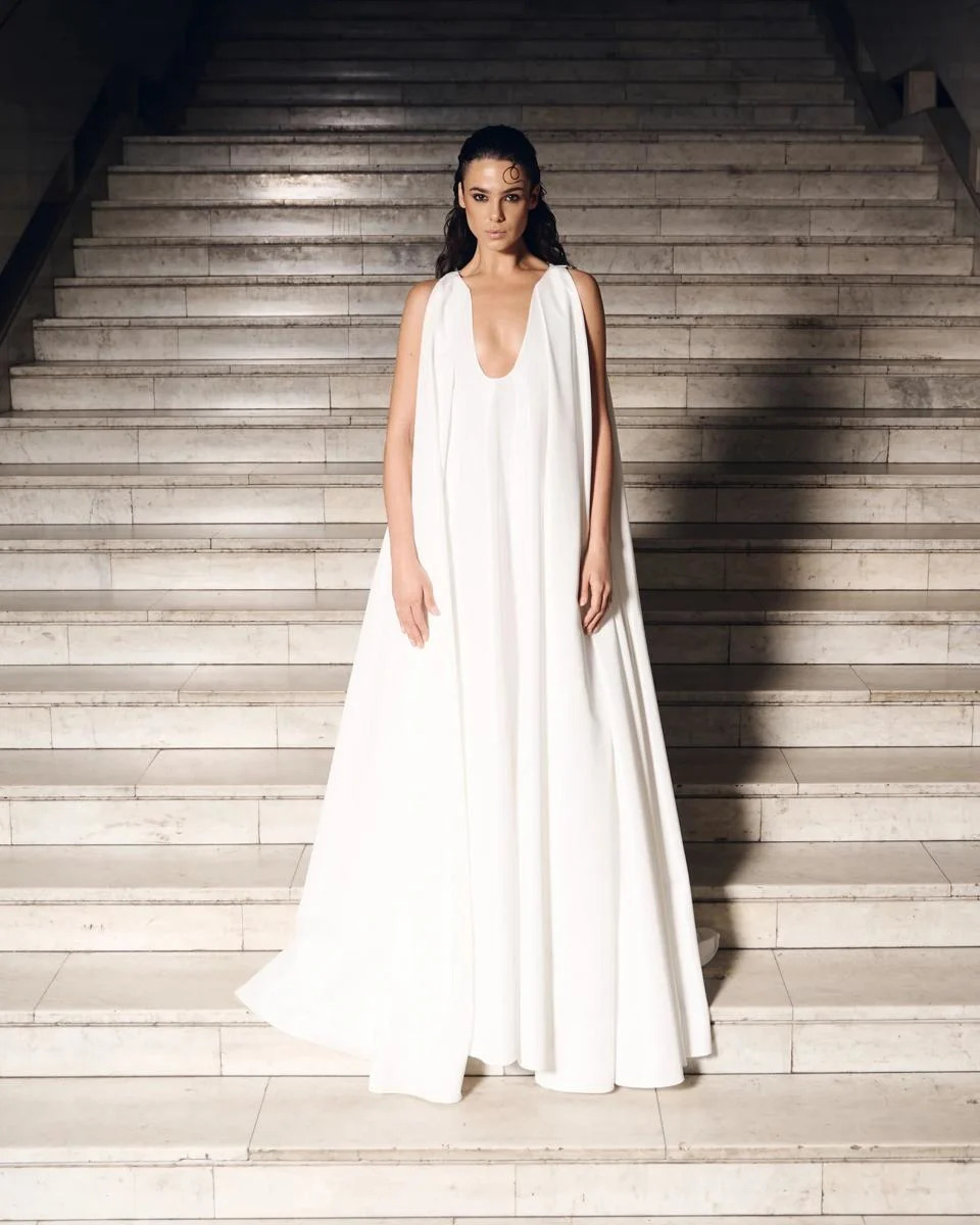 A model wears a voluminous white goddess gown with a deep scoop neck.
